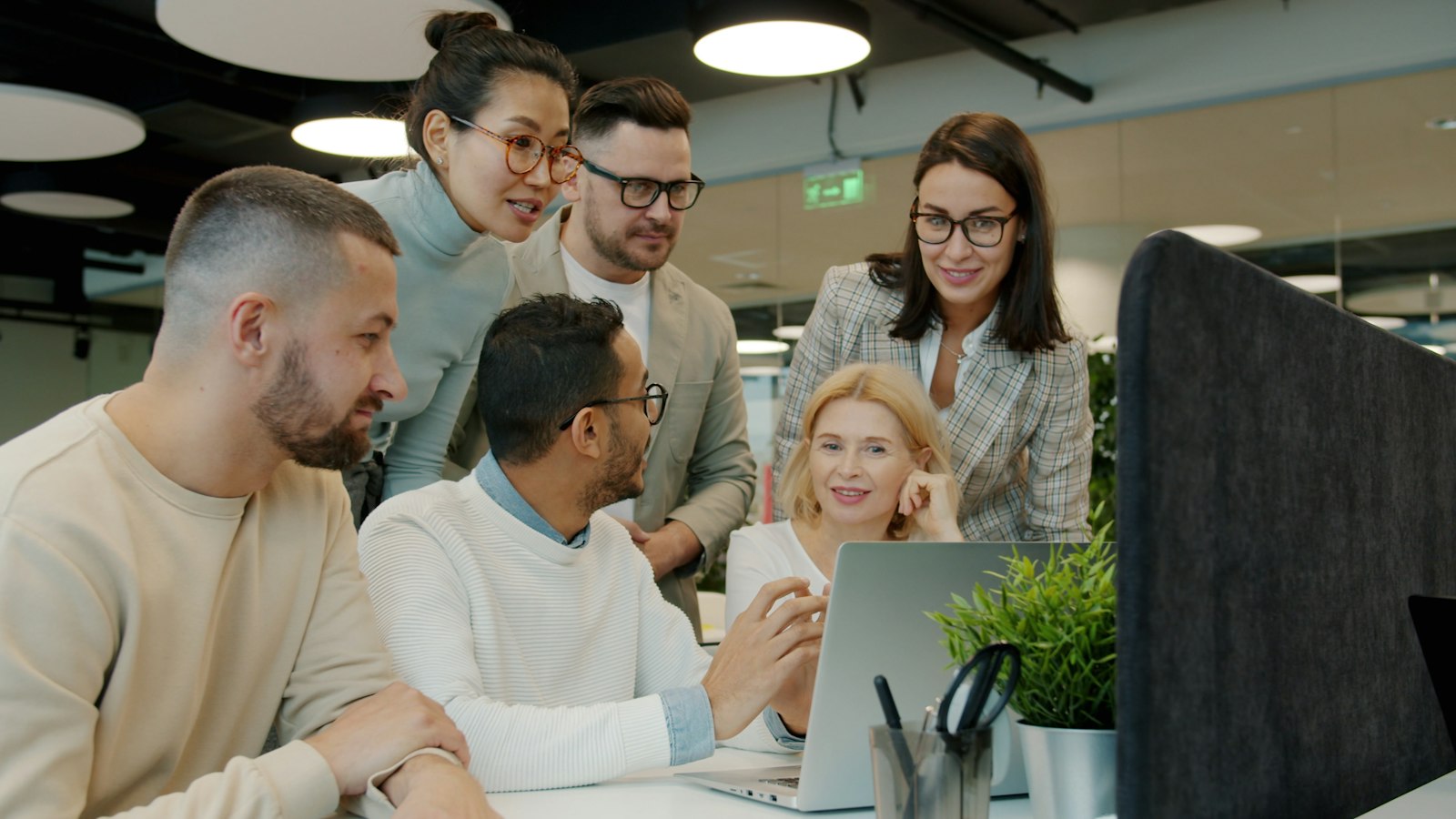 Six colleagues from different backgrounds gathered around a laptop in a modern office