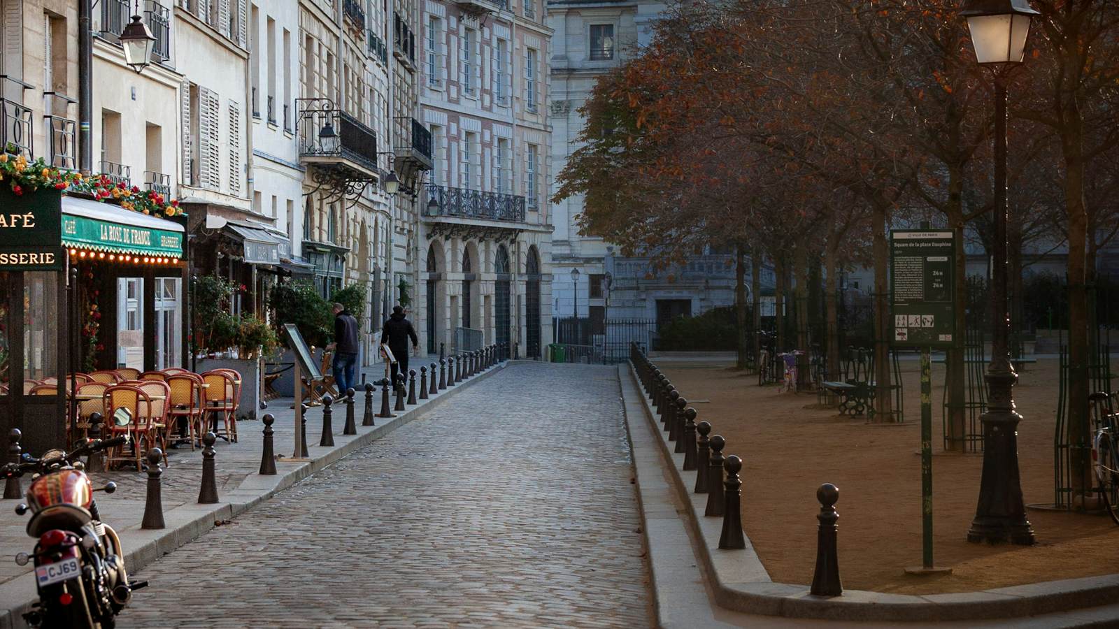 A cobblestone square in Paris lined with cafe tables and lamp posts at dusk